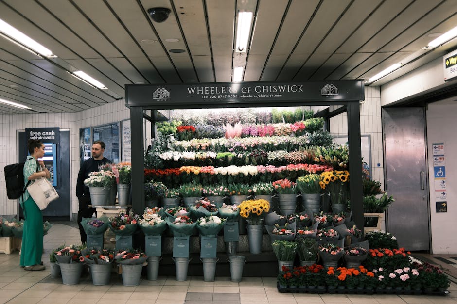 A floral display at Wheeler of Chiswick in an underground station, featuring a variety of fresh flowers arranged in a tiered display with vibrant colors including white, pink, red, yellow, and purple.